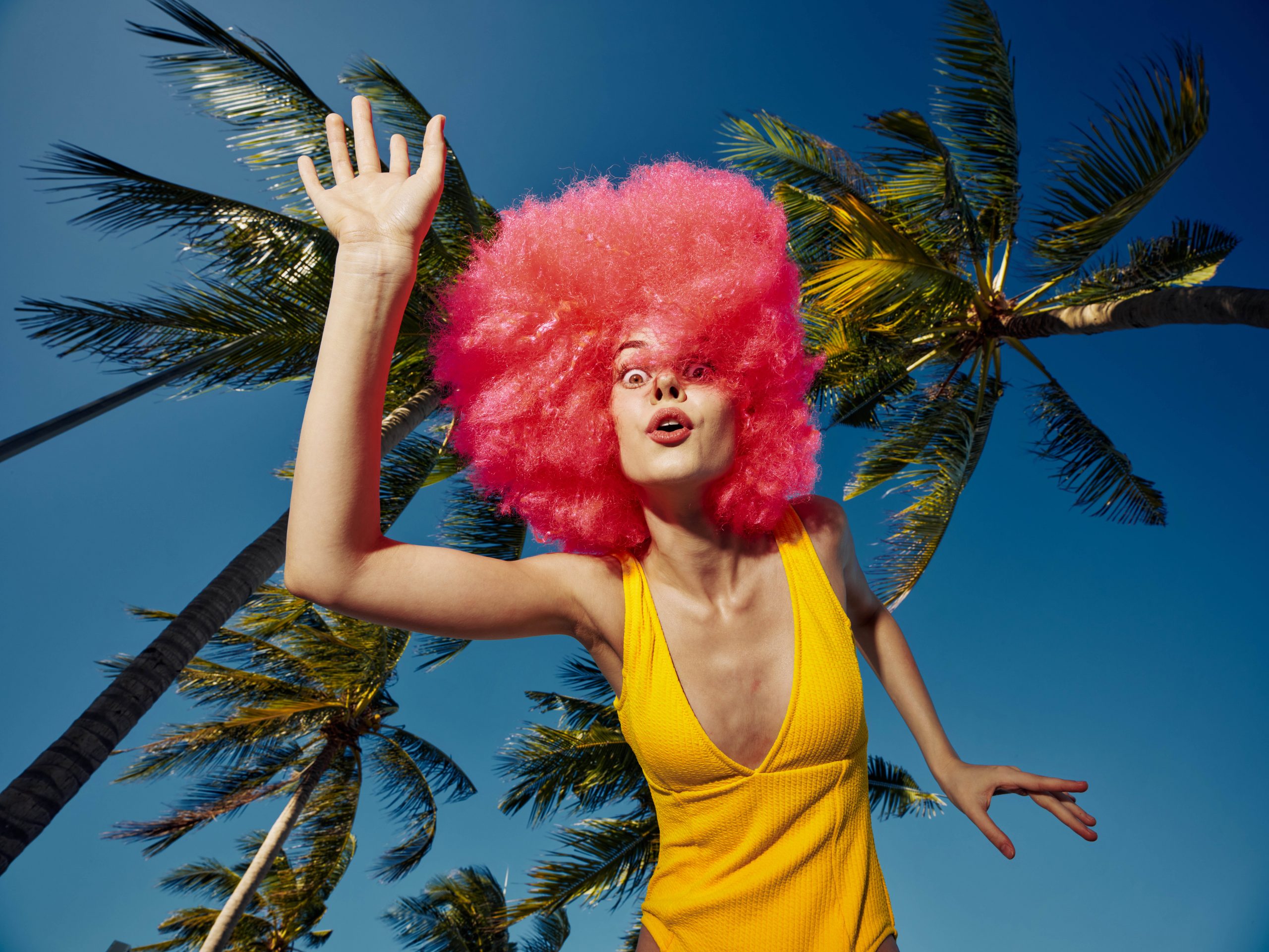Vibrant portrait of a woman in a pink wig and yellow outfit with palm trees, exuding confidence and tropical vibes